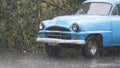 Retro car standing in rain on background of green trees. Action. Small retro car stands under downpour in nature