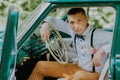 Retro-driver in the vintage car on the outdoor background. Handsome groom in the car. Confident wealthy young man in Royalty Free Stock Photo