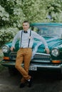 Retro-driver in the vintage car on the outdoor background. Handsome groom in the car. Confident wealthy young man in Royalty Free Stock Photo