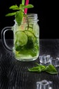 Retro glass jar of lemonade with cucumber and mint on wooden table. Cubes of ice