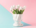 Retro head sculpture with tulip flowers on a pastel blue pink background.