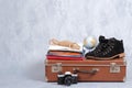 Retro leather suitcase with travel accessories on grey background. Stack of clothes, film photo camera, suede shoes, globe. Travel