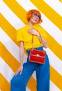 Retro Model holding bag and wearing vintage look on trendy striped yellow background. Minimal fashion spring summer concept. Royalty Free Stock Photo