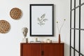 Retro modern compositon of living room interior with design teak commode, black mock up poster frame, book, dried flower in vase.