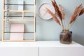 Retro modern decoration wall in the living room with pastel colors, white clock and shelf, modern vase with pampas grass