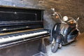 Retro piano near a vintage motorcycle on the background of an old brick black wall Royalty Free Stock Photo