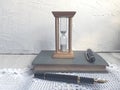 Retro picture of a sand clock on an old book and a pen for taking notes. Wooden table decorated with a handmade tapestry crochet Royalty Free Stock Photo