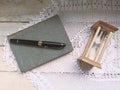 Retro picture of a sand clock on an old book and a pen for taking notes. Wooden table decorated with a handmade tapestry crochet Royalty Free Stock Photo