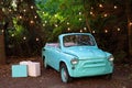 Retro small vintage car standing in garden in summer on a background garland burning bulbs. Classic car Wedding decoration. Decor