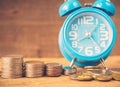 Retro stack of coins and alarm clock on wooden background. Royalty Free Stock Photo