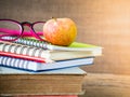 Retro style of apple on stacks of books with pink glasses and red pencil on wooden table background. Royalty Free Stock Photo