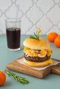 Retro style burger with beef cutlet, cheese and tangerines on a wooden board on a plain background