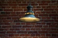 Retro-style ceiling lamp hanging on a metal chain, casting warm light against a rustic brick wall Royalty Free Stock Photo