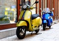 retro style Italian made scooters yellow and blue mopeds. stone paved sidewalk. exterior facade with window