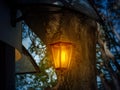 Retro style lantern shines with warm yellow light at dusk. Vintage lantern hangs on a chain under the roof outside the building in Royalty Free Stock Photo