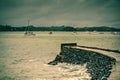 Retro style photo of a curved seawall breaking into stormy sea. Waves crash against the stone wall and into the footpath
