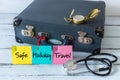 retro style suitcase with compass and medical stethoscope. Colorful sticky notes with the words `Safe, Holiday, Travel`. The conc Royalty Free Stock Photo