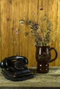 Retro telephone and a bouquet of dried flowers in a clay jug on an old table Royalty Free Stock Photo