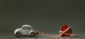 Retro toy car towing wooden red heart on a rope for valentine`s day at the blurred grey background Royalty Free Stock Photo