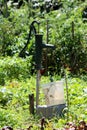 Retro vintage old partially rusted dark green iron hand water pump mounted on metal pipe over plastic bucket in home garden