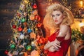 Retro woman with retro hairstyle near the Christmas tree. Young woman in red dress celebrating new year or an event