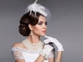 Retro woman portrait. Elegant lady with hairstyle, pearls jewelry set wears in hat and lace gloves posing isolated on studio gray Royalty Free Stock Photo