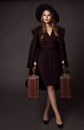 Retro Woman Travel with Suitcase. Elegant Lady in Black Hat holding two Vintage Bags. Old Fashioned Style Model in Classic Dress