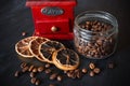 Retro wooden coffee grinder, coffee beans in glass jar and scattered around, four slices of dried lemon, dark surface Royalty Free Stock Photo