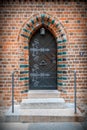 Retro wooden door with ornate iron knocker, handle and hinges in arched entrance with colorful bricks Royalty Free Stock Photo