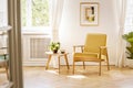 A retro, yellow armchair and a wooden table in a beautiful, sunny living room interior with herringbone floor and white walls. Re