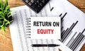 RETURN ON EQUITY text on notebook on chart with calculator and pen