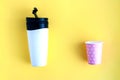 Reusable black and white takeaway coffee cup with disposable paper cup isolated on yellow background Royalty Free Stock Photo