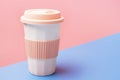 Reusable ceramic glass for coffee with silicone lid on pink and blue background.