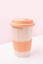 Reusable ceramic glass for coffee with silicone lid on pink and white background.