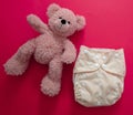 Reusable cloth baby diaper. Eco friendly nappy and teddy bear on red background