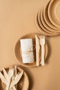 Brown craft disposable bag and tableware cup, plate, and wooden fork, knife on brown background flat lay top view Royalty Free Stock Photo