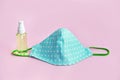 Reusable homemade fabric mask for the face and a sanitizer spray bottle. pink background