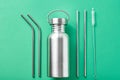 Reusable plastic free items on a green background. Top view of aluminun bottle and metal tubes. Zero waste eco friendly concept