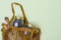 A reusable string bag contains two wooden spoons and two glass jars of tea on a mint background. Reusable concept, environmental