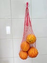 Reusable thread mesh filled with oranges hanging on the ceramic tiles wall. Home storage for future use Royalty Free Stock Photo