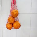 Reusable thread mesh filled with oranges hanging on the ceramic tiles wall. Home storage for future use Royalty Free Stock Photo