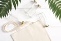 A reusable woven bag and glass bottles lie on a white background, near green leaves