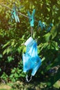 Reused and broken disposable medical mask dries forgotten on clothesline in garden.