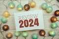 Review 2024 text on paper card with LED cotton balls top view on wooden background