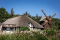 Revitalized wattle and daub house with thatched roof and a wooden windmill in Niechorze, Poland. . Royalty Free Stock Photo