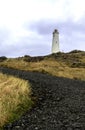 Reykjanes Lighthouse, Iceland. A white lighthouse perched atop a hill,surrounded by yellow grass fields and a dirt road