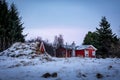 A red wooden icelandic house and a traditional turf cellar in the winter forest.