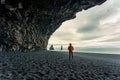 Reynisdrangar natural rock formation with female tourist standing in halsanefshellir cave on black sand beach in summer at Iceland