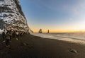 Reynisfjara black sand beach at sunset and the basalt formations covered in snow and illuminated by the last rays of the sun from