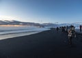 Reynisfjara black sand beach at sunset illuminated by the last rays of the sun from the horizon of the sea with tourists amazed